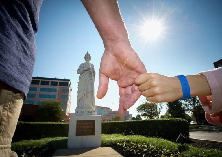 St. Jude Image of child holding adults hand in front of St. Jude Statue