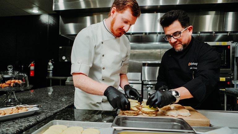Two Chefs in kitchen one in black coat one in white