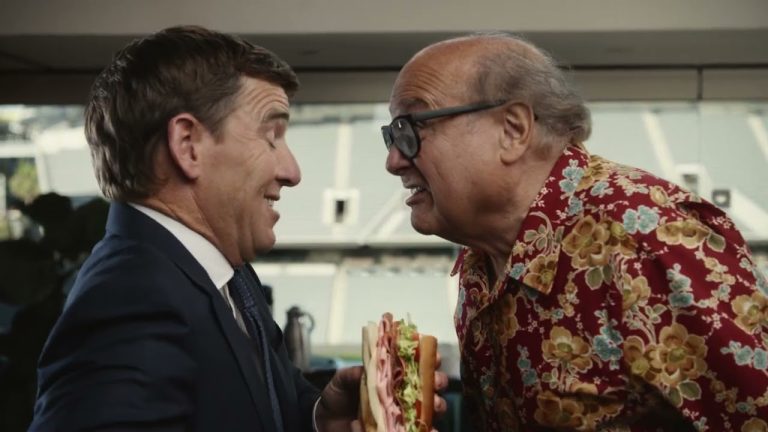 Eli Manning and Danny DeVito in Jersey Mike’s NFL campaign, standing with sub sandwiches in a lighthearted rivalry.